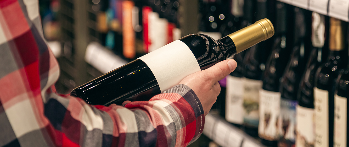 Osoba w sklepie ogląda etykietę znajdującą się na butelce wina.